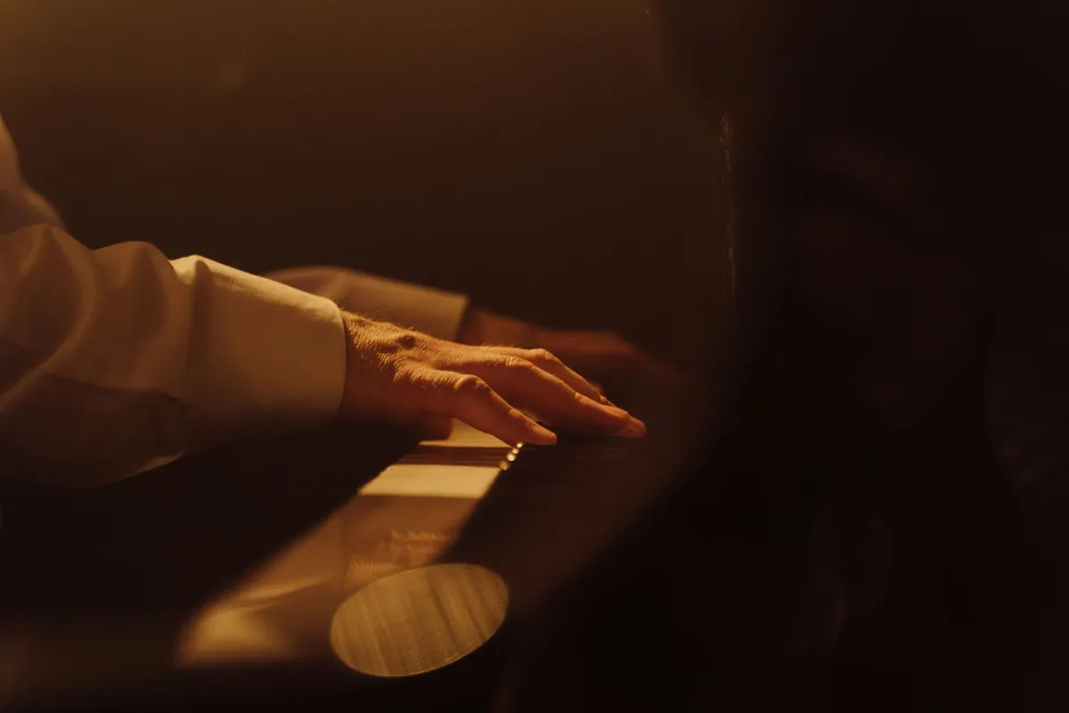 A pianist's hand on the keys of a piano in warm amber light