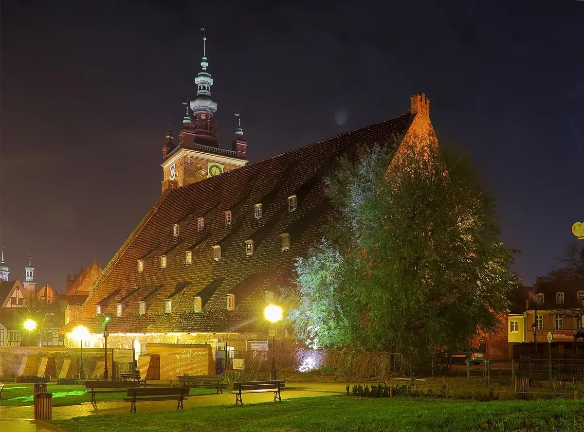 The huge steep roof of the Great Mill in Gdańsk lit from below at night, with the tower of St Catherine's Church rising behind it